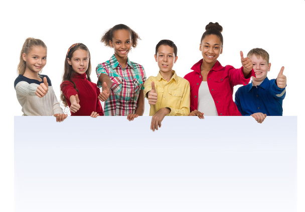 niños de diferente tez sosteniendo un vacío en blanco con los pulgares hacia arriba
 - Foto, Imagen