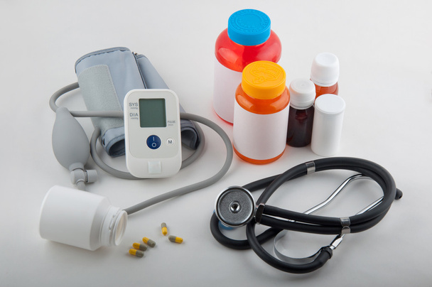 Harmaa lääketieteellinen tonometri, fonendoskooppi, pillerit ja lääkepullot valkoisella
 - Valokuva, kuva