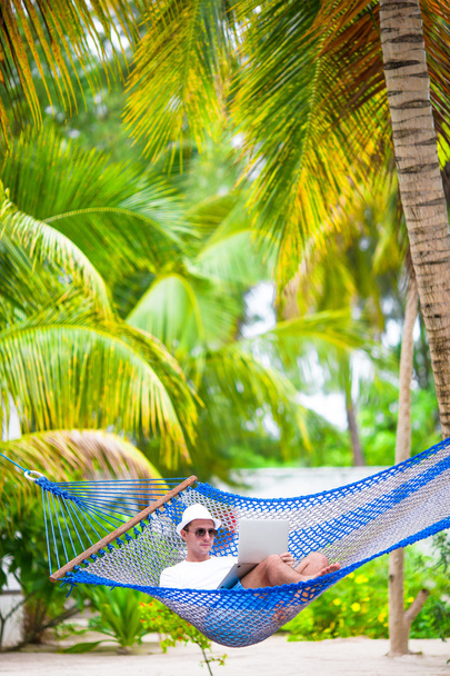 Hombre joven con el ordenador portátil en la hamaca en vacaciones tropicales - Foto, Imagen