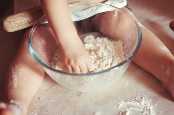 little scullion is kneading dough in an apron and chef's hat sitting in the flour. - Foto, afbeelding