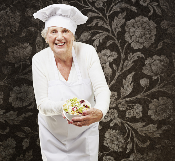 Femme âgée cuisinier tenant un bol avec salade contre une ba vintage
 - Photo, image