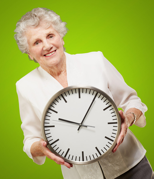 retrato de uma mulher idosa feliz segurando relógio sobre verde
 - Foto, Imagem