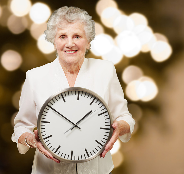 Retrato de una mujer mayor feliz sosteniendo el reloj contra un abstracto
 - Foto, imagen