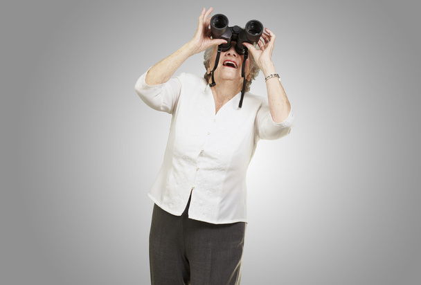 Portrait of senior woman looking through a binoculars against a - Photo, Image