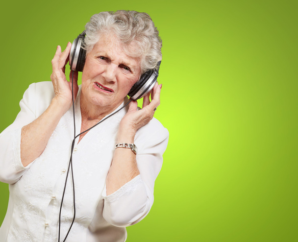 Portrait of senior woman listening to music over green backgroun - Photo, Image