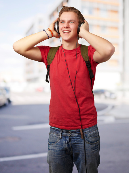Портрет жизнерадостного молодого студента, слушающего музыку с хэдфоном
 - Фото, изображение