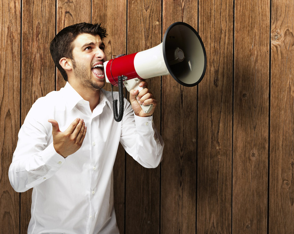 Portret van jonge man schreeuwen met megafoon tegen een houten w - Foto, afbeelding