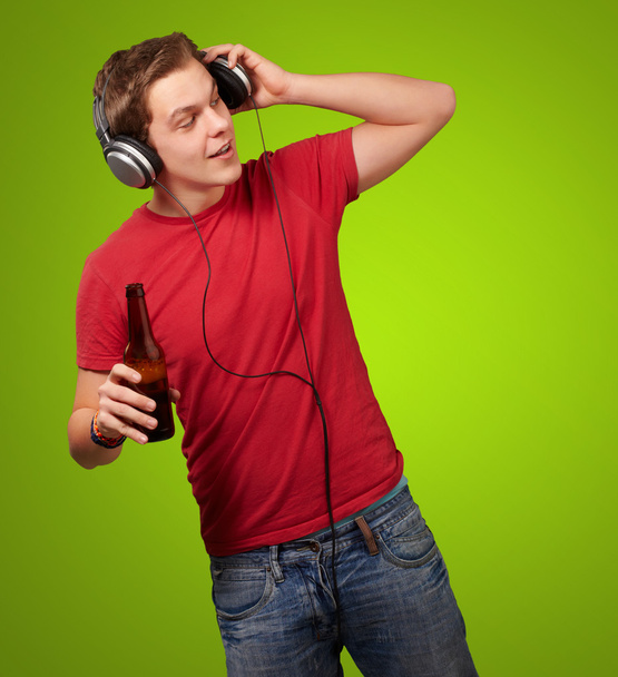 Portrait of young man listening music and holding beer on green - Photo, image
