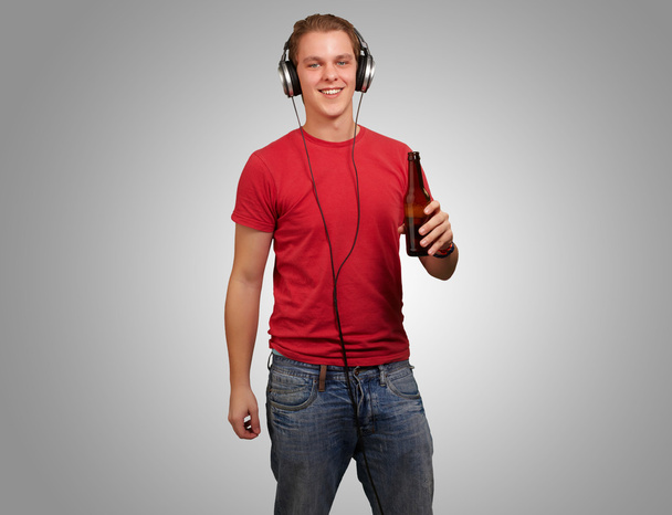 Portret van jonge man muziek luisteren en bier bedrijf over grijs - Foto, afbeelding