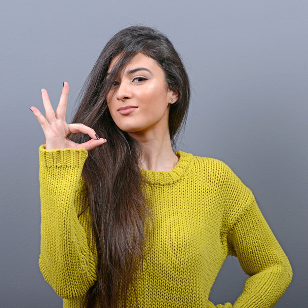 Portrait of happy woman showing ok sign against gray background - Foto, afbeelding