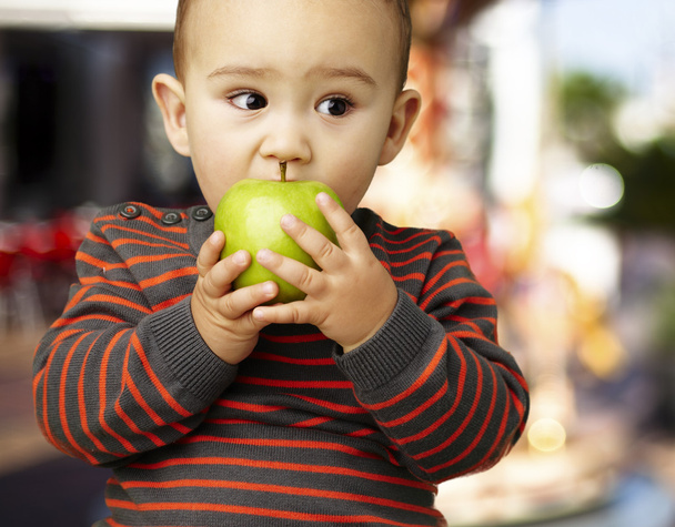 Portrait of a handsome kid bitting a green apple against a carou - Photo, Image