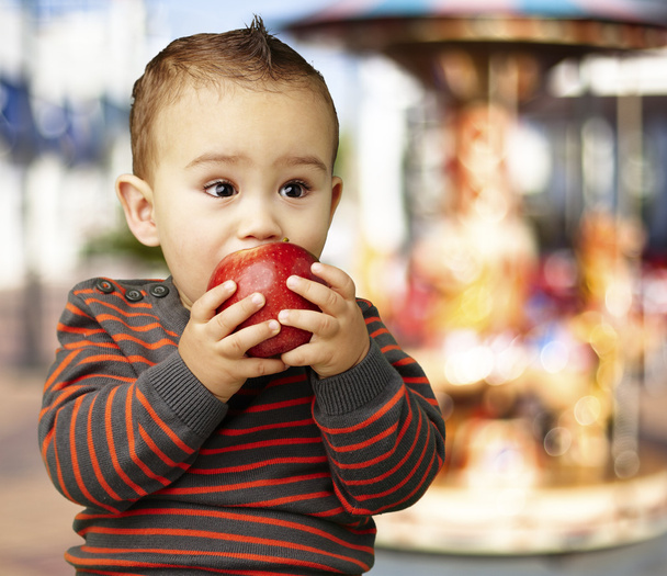 Portret van een knappe jongen zuigen een rode appel tegen een carouse - Foto, afbeelding