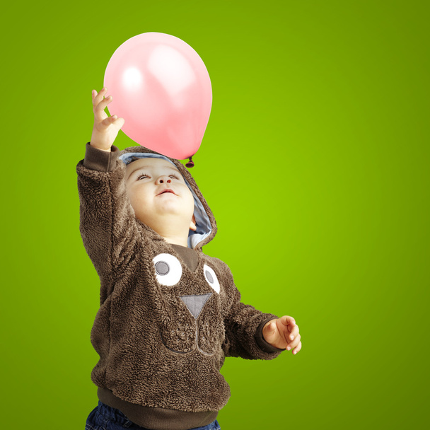Porträt eines lustigen Kindes, das versucht, einen rosafarbenen Luftballon über ein grünes B zu halten - Foto, Bild