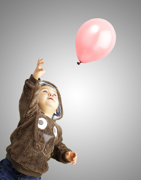 Portrait of funny kid trying to hold a pink balloon over grey ba - Fotoğraf, Görsel