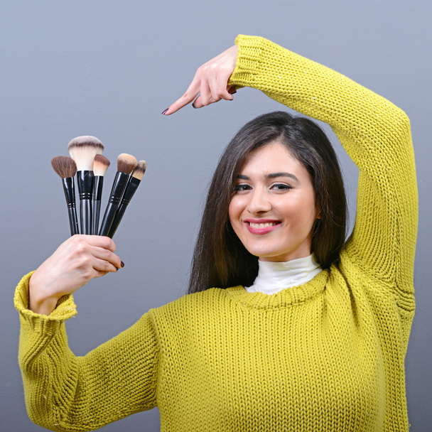 Portrait of woman holding make-up brushes against gray backgroun - Fotoğraf, Görsel
