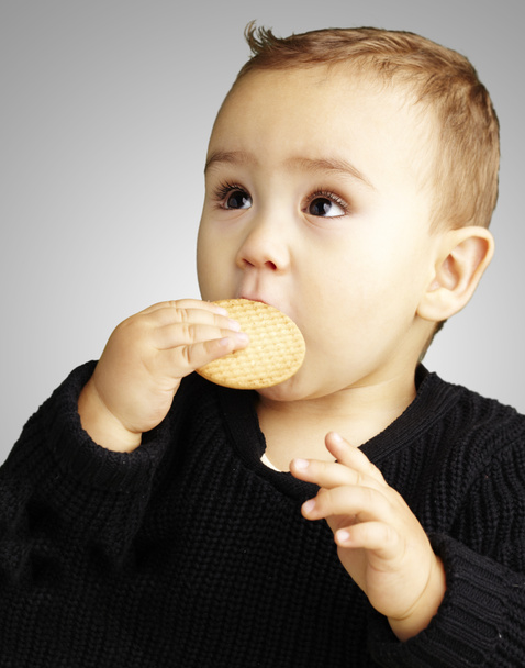 Portrait of kid eating a biscuit over grey background - Foto, Bild
