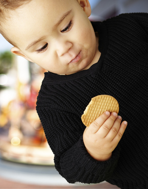Portrait of handsome kid eating a biscuit against a carousel - Foto, Bild