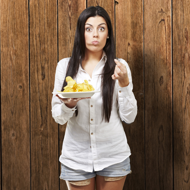 Young woman eating potatoe chips against a wooden background - Photo, Image