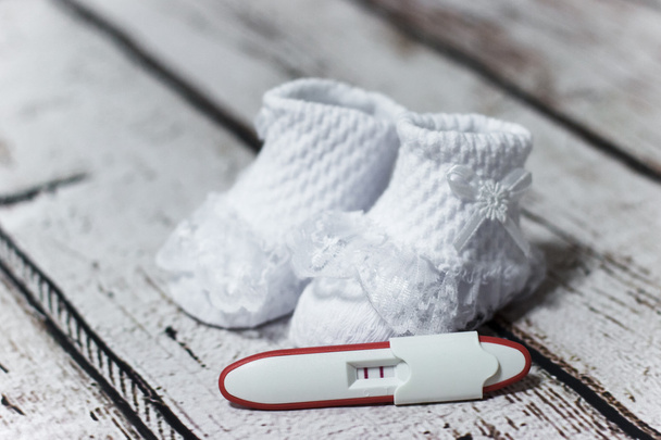 Young woman holding baby shoes and positive pregnancy test - Photo, Image