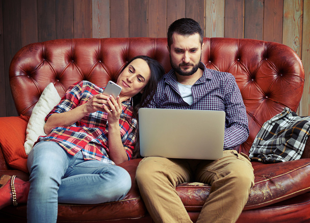 couple sitting on sofa and using gadgets - Foto, imagen