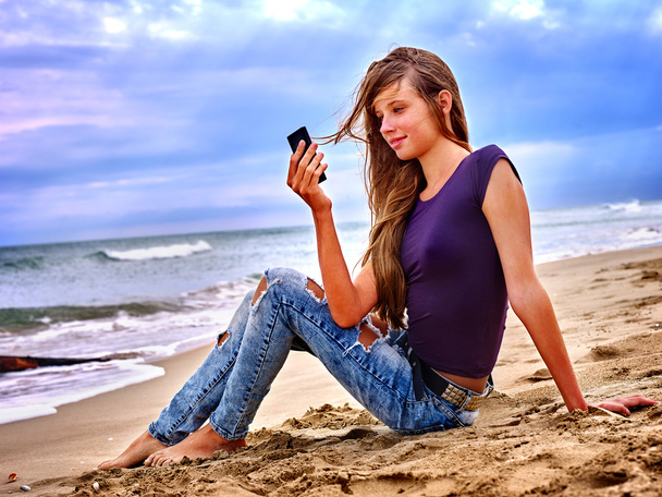 Cep telefonu kum deniz kenarında oturan kızla. - Fotoğraf, Görsel