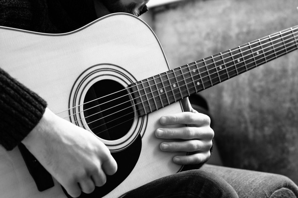 joven tocando una guitarra acústica en el fondo de una pared de hormigón
 - Foto, imagen