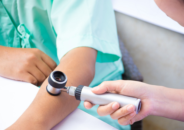 Лікар перевіряє шкіру за допомогою дерматоскопа на руці людини
 - Фото, зображення