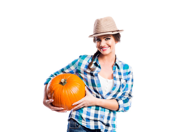 Woman in blue checked shirt, hat holding orange pumpkin - Fotografie, Obrázek