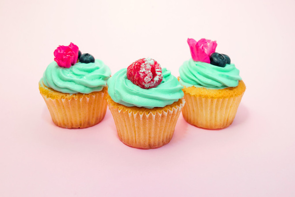 Cupcakes z masłem śmietany i wanilii z malin i jagód z różowymi kwiatami na różowym tle - Zdjęcie, obraz