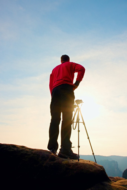 Professional photographer takes photos with camera on tripod on rocky peak. Dreamy spring landscape. - Photo, Image