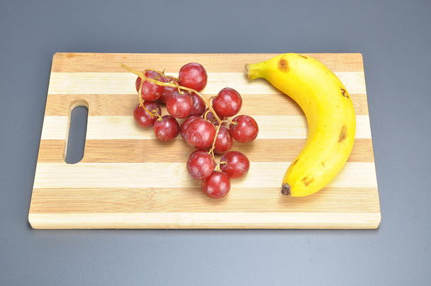 Delicious bunch red seedless crimson grape and banana on bamboo  - Photo, Image
