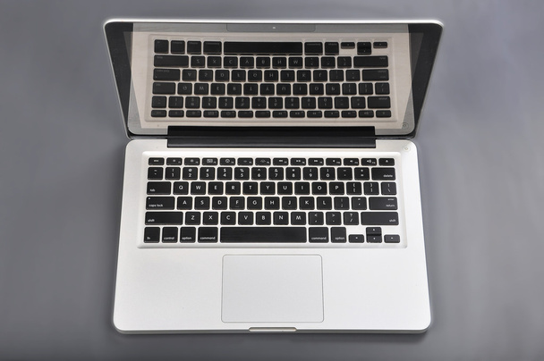 Ασημένια laptop με μαύρο κουμπί σε γκρι φόντο - Φωτογραφία, εικόνα