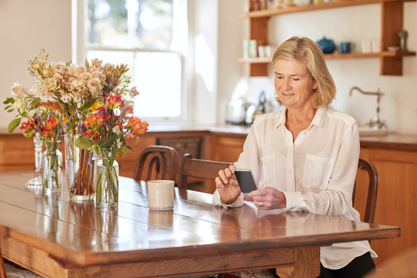 woman reading message on phone in kitchen - Zdjęcie, obraz
