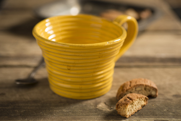Άδειο κίτρινο φλυτζάνι τσαγιού μεταξύ κουτάλι και μπισκότα - Φωτογραφία, εικόνα