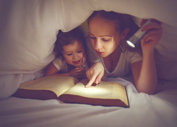Οικογενειακή ανάγνωση τον ύπνο. Μαμά και παιδί ανάγνωση βιβλίων με ένα flashl - Φωτογραφία, εικόνα