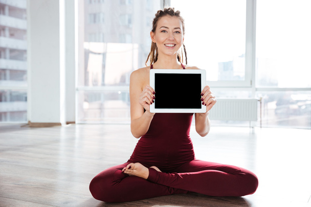 Happy woman sitting in yoga pose showing blank screen tablet - Foto, imagen