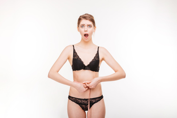 Shoked beautiful young woman in lace lingerie measuring her waist - 写真・画像