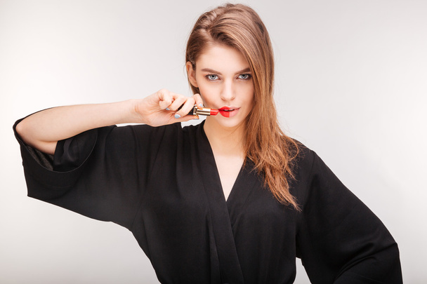 Gorgeous woman demonstrating red lipstick on half of her lips - 写真・画像