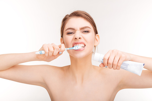 Portrait of beautiful woman holding toothpaste and brushing her teeth - Foto, afbeelding