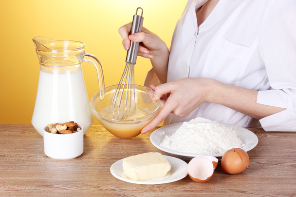 Female hands mixing eggs in bowl on wooden table on yellow background - Valokuva, kuva
