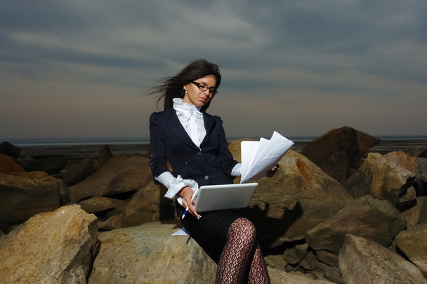 曇り空を背景に、海で岩の上に座っている女性のビジネス. - 写真・画像