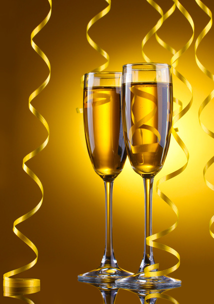 Glasses of champagne and streamer on yellow background - 写真・画像