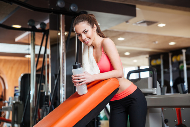 Happy sportswoman with bottle of water on training in gym  - Фото, изображение