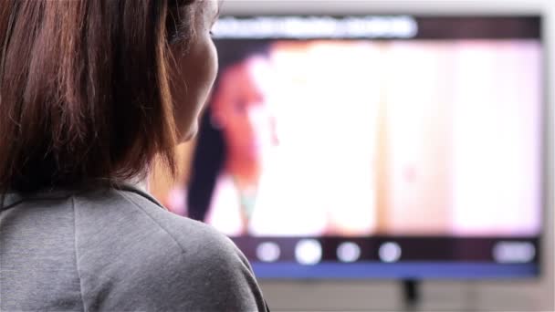 Fiatal nő távirányítóval tv-t néz - Felvétel, videó
