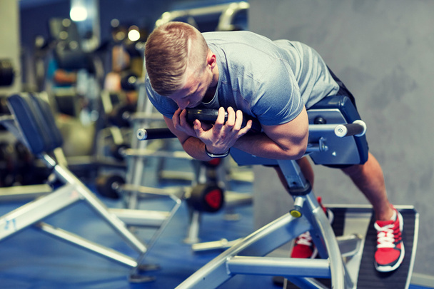 young man flexing back muscles on bench in gym - Foto, Imagen