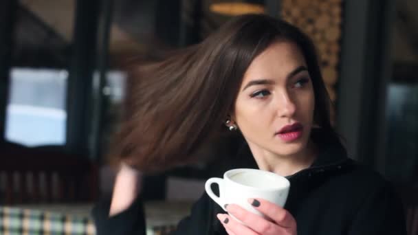 sehr süßes und schönes Mädchen trinkt Kaffee und schaut in die Kamera. das Mädchen im Café. - Filmmaterial, Video
