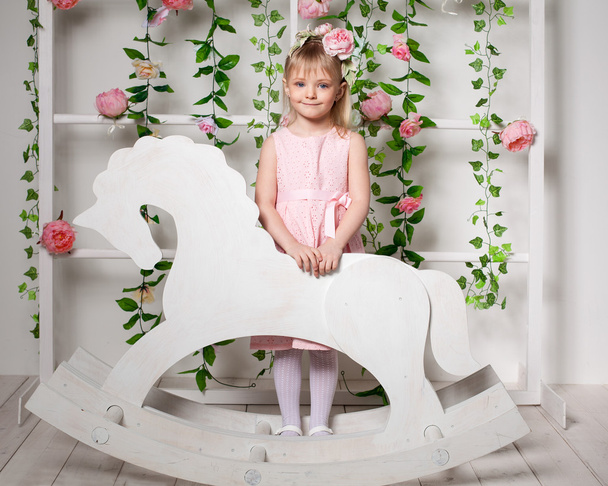 Portrait of a little blonde girl  standing near the wooden horse - Photo, Image
