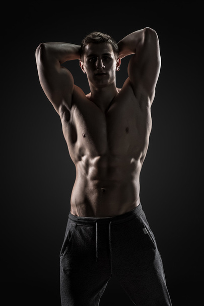 Sexy shirtless bodybuilder posing, looking at camera on black background. - Fotó, kép