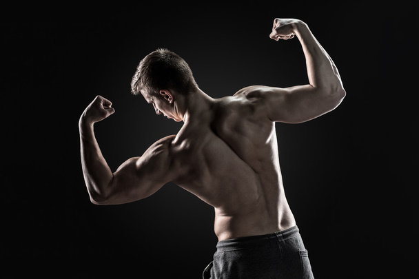 Zadní pohled svalnatý mladík ukazující zpět, biceps svaly - Fotografie, Obrázek