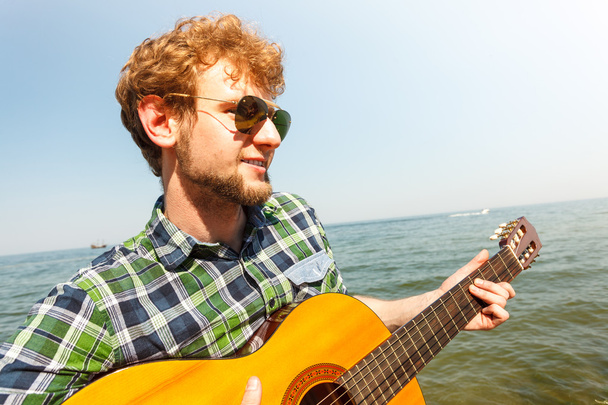 Young man hipster playing guitar by sea ocean. - Zdjęcie, obraz